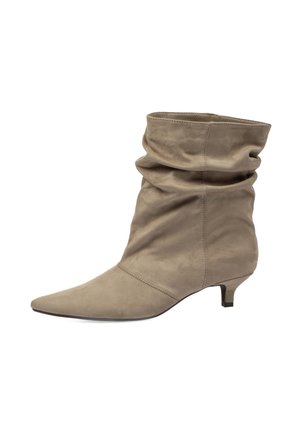 Bota de ante beige hasta la mitad de la pantorrilla con puntera puntiaguda, parte superior holgada y tacón bajo estilo kitten mirando hacia la derecha sobre fondo blanco.