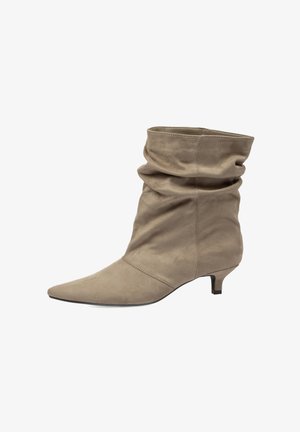 Bota de ante beige hasta la mitad de la pantorrilla con puntera puntiaguda, parte superior holgada y tacón bajo estilo kitten mirando hacia la derecha sobre fondo blanco.