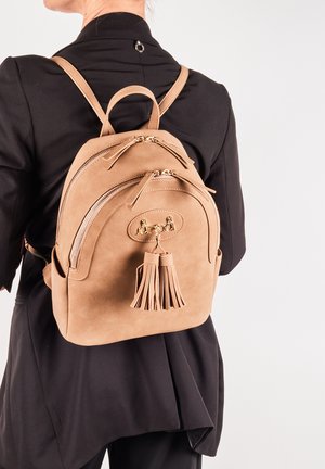 Sac à dos en suède tan avec double zip, accessoires dorés, un patch en cuir, et un détail en frange. Bretelles réglables et forme arrondie.
