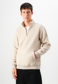 Beige fleece pullover med halv lynlås, kængurulomme og ribbede manchetter. Blød tekstur med en afslappet pasform.