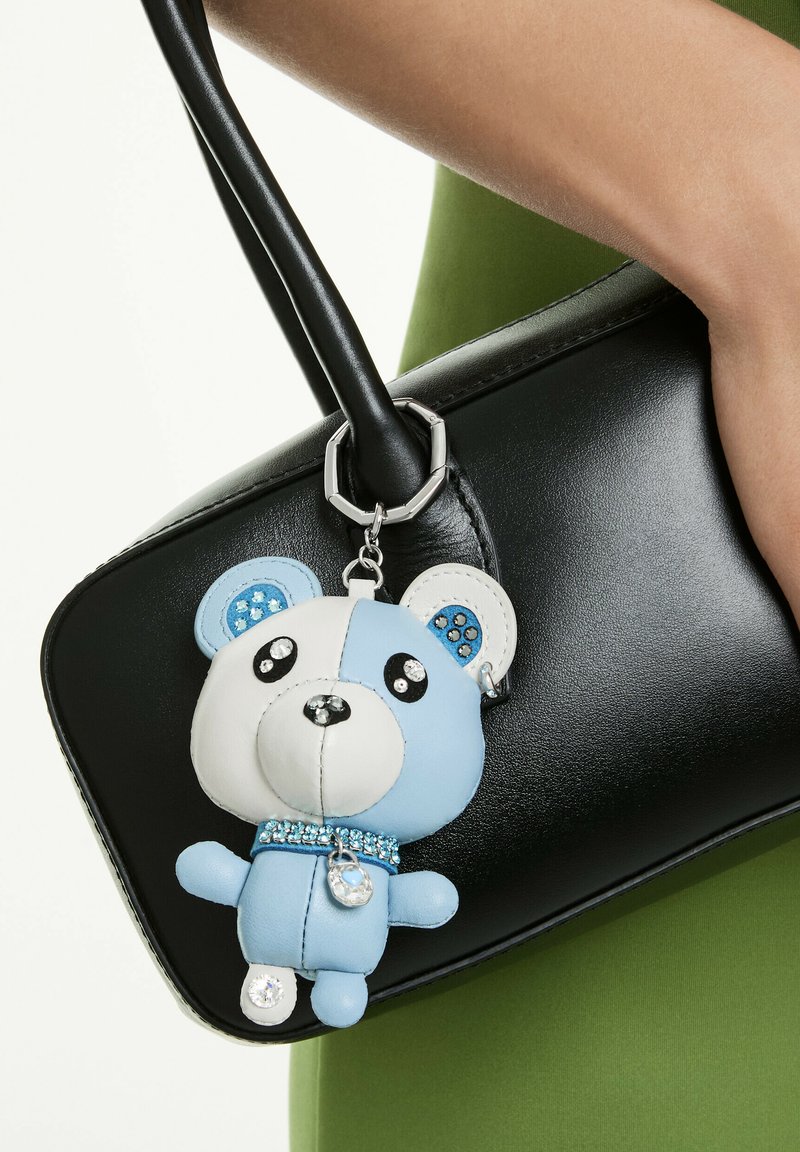 Sac à main noir avec une texture en cuir lisse, agrémenté d'un porte-clés ours bleu et blanc décoré de strass et d'un charm argenté.