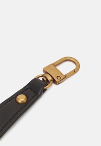 Sangle en cuir noir avec un clip à pression en laiton, présentant un détail en stud doré, une texture lisse et une forme de clip rectangulaire.