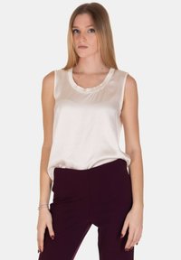 Top senza maniche color crema in satin con scollatura rotonda. Il tessuto ha una texture liscia e una leggera lucentezza. Abbinato a pantaloni viola scuro.