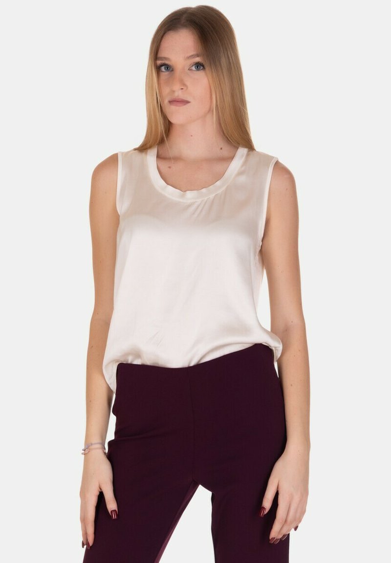 Top senza maniche color crema in satin con scollatura rotonda. Il tessuto ha una texture liscia e una leggera lucentezza. Abbinato a pantaloni viola scuro.