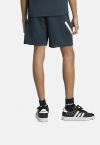 Marineblauwe sportshorts met witte zijstreep, gecombineerd met zwarte sneakers met drie witte strepen en zwarte enkelkousen.