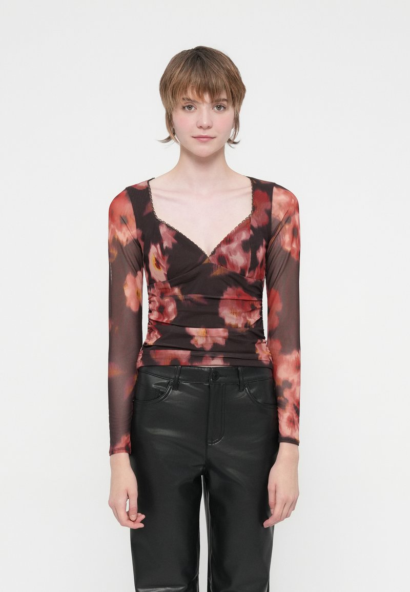 Bluză cu mânecă lungă, transparentă, cu model floral, având un design ajustat, decolteu adânc în formă de V și textură plisată în nuanțe de roșu, roz și negru. Asortată cu pantaloni negri.