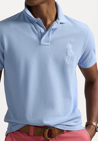 Light blue polo shirt with a textured fabric, featuring a three-button collar and an embroidered logo on the left chest.