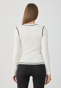 Žebrovaný top s dlouhým rukávem v off-white barvě s kontrastními černými švy, přiléhavý střih a kulatý výstřih. Nosen s černými džíny.