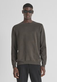 Maglione marrone con texture, scollo a girocollo, polsini e orlo a coste. Il modello indossa occhiali da sole rettangolari neri e pantaloni neri.