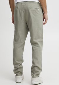 Light olive green linen pants with a relaxed fit, featuring back pocket detail and subtle texture. Paired with white sneakers.