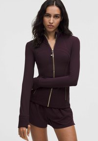 Burgundi värvi lukuga jakk pikade varrukatega, kuldsed detailid ja sobiv disain. Kombineeritud sobivate lühikeste pükstega, mis on valmistatud siledast ja venivast kangast.