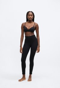 Sort bh og leggings med høj talje, begge lavet af glat stof. Bhen har tynde stropper og dyb udskæring; leggings er tætsiddende og går til anklerne.