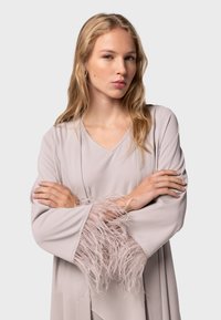 Lys beige omslagskjole med lange ærmer, med teksturerede fjerdetaljer ved manchetterne. Glat stof, V-hals design.