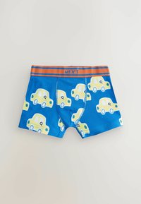 Blå boxershorts med et mønster af gule tegneserie biler, med en orange talje, der er mærket "NEXT." Lavet af bomuldsstof.