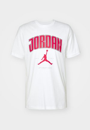 Balta medvilnė marškinėliai su ryškiai raudonu "JORDAN" tekstu ir raudonu Jumpman logotipu. Trumpi rankoviai ir klasikinė apvalia kaklo iškirpte.