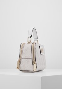 Petit sac à main designer beige et blanc avec deux zips dorés, une courte poignée blanche et un motif logo subtil sur une surface lisse.