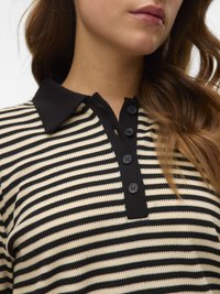 Donna che indossa un top in maglia orizzontale a strisce nere e beige con un colletto nero e quattro bottoni neri sulla patta.