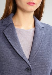 Marintröja i randigt mönster med en texturerad tyg, slagkrage och en enda svart knappknäppning. Bärs över en ljusgrå topp.