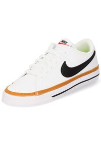 Zapatilla blanca de cuero con el logo de swoosh negro, costuras naranjas alrededor de la suela y una suela de goma. Cuenta con cierre de cordones.