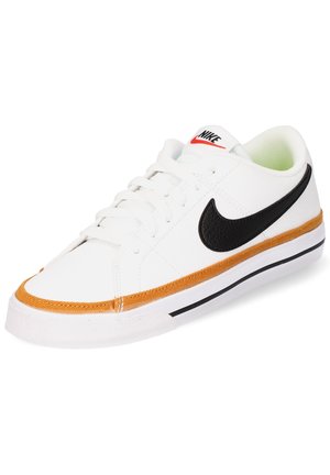 Zapatilla blanca de cuero con el logo de swoosh negro, costuras naranjas alrededor de la suela y una suela de goma. Cuenta con cierre de cordones.