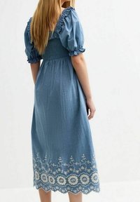 Modrá šambray šaty s nabíranými rukávy, smockovaným živůtkem a bílou květinovou výšivkou podél lemu. Délka do půli lýtek, měkká textura.