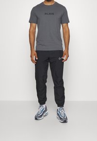 Grå T-shirt med rund hals och svart text "PARIS", i kombination med svarta sweatpants och grå sneakers med blå detaljer och vita inslag.