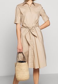 Beige skjortklänning med knyt i midjan, korta ärmar och knäppning fram. Åtföljd av en liten vävd halmvecka med svart inredning.