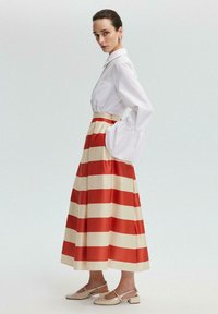 White button-up shirt with puff sleeves paired with a long, striped skirt in red and cream. Model wears beige slingback shoes.