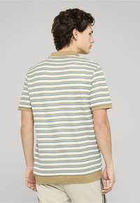 Polo à manches courtes tricoté en rayures blanches, olive et bleues. Présente un col rond et un tissu texturé avec bordures côtelées.