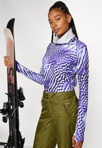 Pikkade varrukatega lilla särk, millel on laineline muster ja kõrge krae; koos oliivroheliste lumeülikonnaga, millel on lukuga taskud ja kahe nupuga kinnitamine.