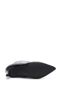 Zapato de cuero negro con punta afilada, con una textura suave y un tacón delgado. La suela es plana y tiene un patrón acanalado para mayor tracción.