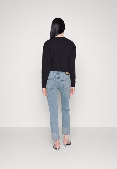 Sweat-shirt noir court, jean bleu clair avec des poignets repliés, et sandales à talons noires. Design simple sans motifs ni accents visibles.