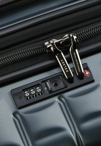 Valigia rigida nera con texture a righe, dotata di un meccanismo di chiusura approvato dalla TSA e doppie zip metalliche.