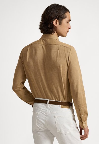 Koszula z długim rękawem w kolorze brązowym o jodełkowym wzorze, z klasycznym kołnierzykiem. Posiada mankiety na guziki oraz gładką fakturę, zestawiona z białymi spodniami i brązowym paskiem.