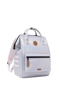 Rucksack aus schimmerndem hellgrauem Material, mit einer vorderen Reißverschlusstasche, zwei Griffen und verstellbaren rosa Trägern sowie einem Logo-Patch oben.