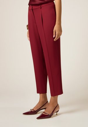 Pantaloni su misura bordeaux con pieghe, vita alta e tasche laterali, abbinati a décolleté slingback in vernice bordeaux con dettagli argento.