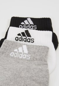 Tres pares de calcetines deportivos en negro, blanco y gris, con el logo de Adidas. Están hechos de una mezcla de algodón y tienen puños acanalados.