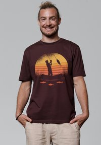 Bordeaux katoenen T-shirt met een grafisch ontwerp van een visscène met een zonsonderganggradiënt, silhouet van een visser en oranje visdetails. Korte mouwen, ronde hals.