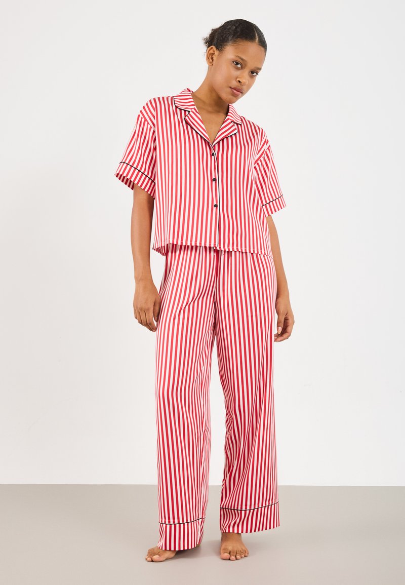 Red and white striped pajama set featuring a short-sleeve top with a collar and pants with wide legs and black trim at cuffs.