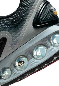 Zapatilla negra y gris que presenta una parte superior de malla texturizada, una unidad de amortiguación prominente con burbujas de aire transparentes y una suela con patrón de diamantes.