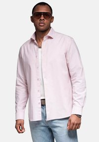 Lichtroze overhemd met knopen van katoen, gecombineerd met een witte tanktop, lichtblauwe jeans en oversized bruine zonnebril.