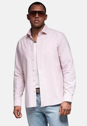Light pink button-up shirt made of cotton, paired with a white tank top, light blue jeans, and oversized brown sunglasses.