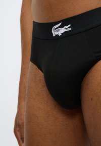 Μαύρα βαμβακερά εσώρουχα με λεία υφή, που διαθέτουν αντίθετο λευκό κεντημένο λογότυπο κροκόδειλου στη μέση.