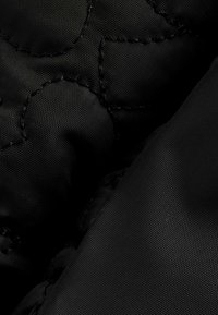 Material textil negru, matlasat, cu o textură netedă, având modele de cusături proeminente și un aspect durabil. Moale și ușor umplut.