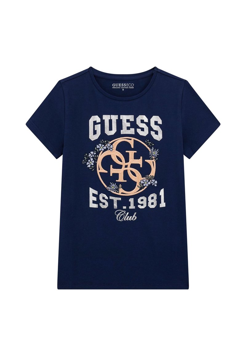 Tumesin sinise puuvillase T-särgiga, millel on valge ja persikavärvi graafiline tekst "GUESS EST.1981 Club" lillemotiividega ning ümmargune kaelus.