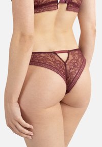 String en dentelle bordeaux avec des motifs floraux, texture semi-transparente et détail découpé à l'arrière, orné de finitions délicates et de bretelles.