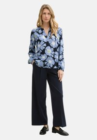 Blauwe bloemenblouse met lange mouwen, v-hals en zwarte broek. De blouse heeft lichtblauwe en witte bloemen en een relaxte pasvorm.