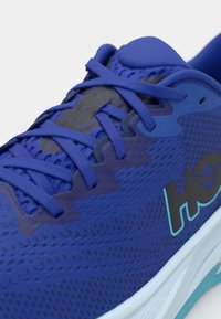 Blauwe hardloopschoen met een textuur van gaas bovenwerk, platte veters en een witte zool. Heeft subtiele branding en een gewatteerde kraag voor comfort.