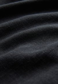 Sort stof med blød tekstur, der har subtile folder og en glat overflade, hvilket antyder et let materiale.