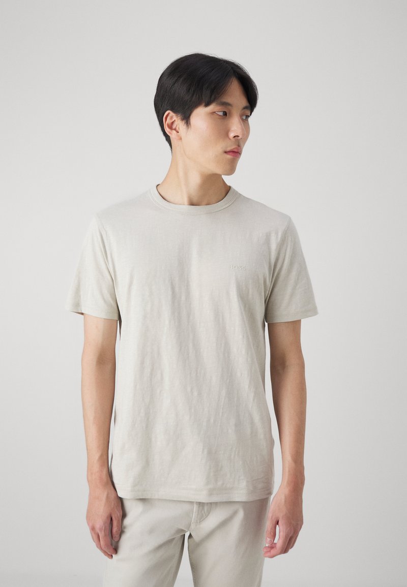 Ljusbeige t-shirt med rund halsringning i mjukt, strukturerat tyg. Har korta ärmar och en liten logga på bröstet. Enkelt utförande.